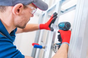 Steel stud wall install by worker with safety glasses and power tool.